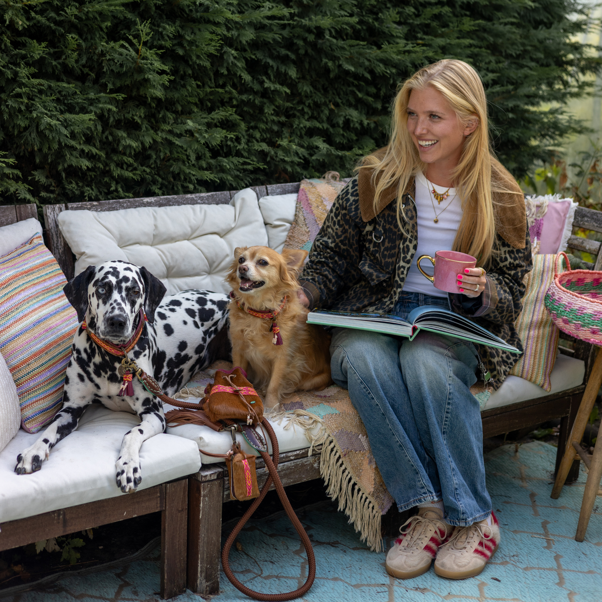 Vrouw op een bank met Yuki beloningsbuidel en Yuki poepzakjeshouder aan een Rover touwriem, naast een Dalmatiër en een kleine hond met Yuki halsbanden