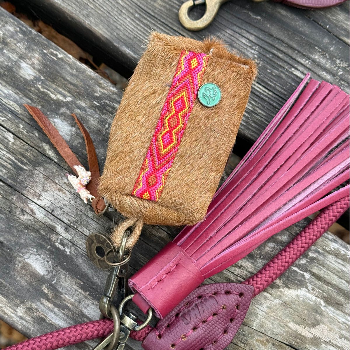 Yuki poepzakjeshouder met roze boho band naast een bordeauxrode Yuki charm en touwriem op een houten bank