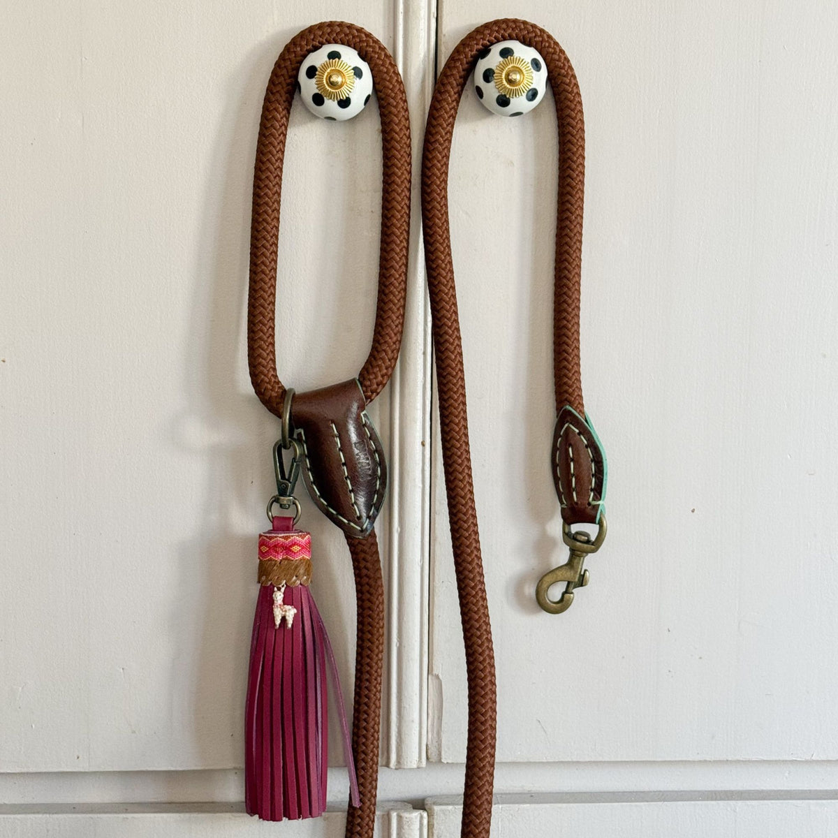Twee bruine touwriemen aan een kastdeur, één met de bordeauxrode Yuki charm met lama-bedeltje aan de riem